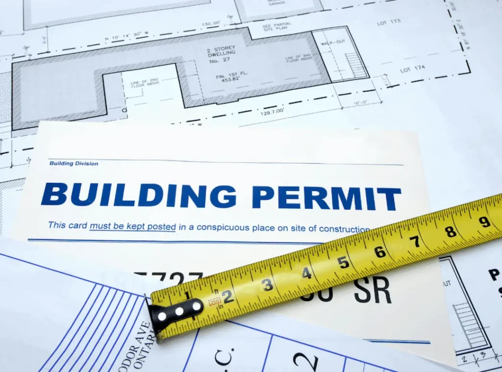 Building permit document with construction site plans, property layout drawings, and measuring tape for residential development.