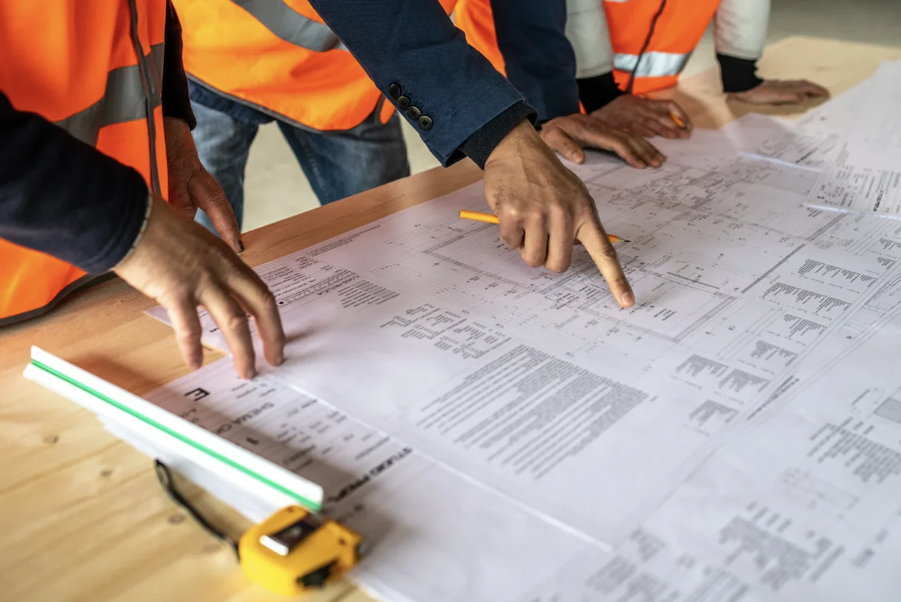 Engineers and construction workers examining architectural blueprints during a commercial building project.