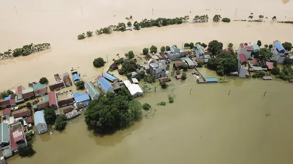 Aerial view of a flooded residential area with houses surrounded by rising floodwater after a natural disaster.